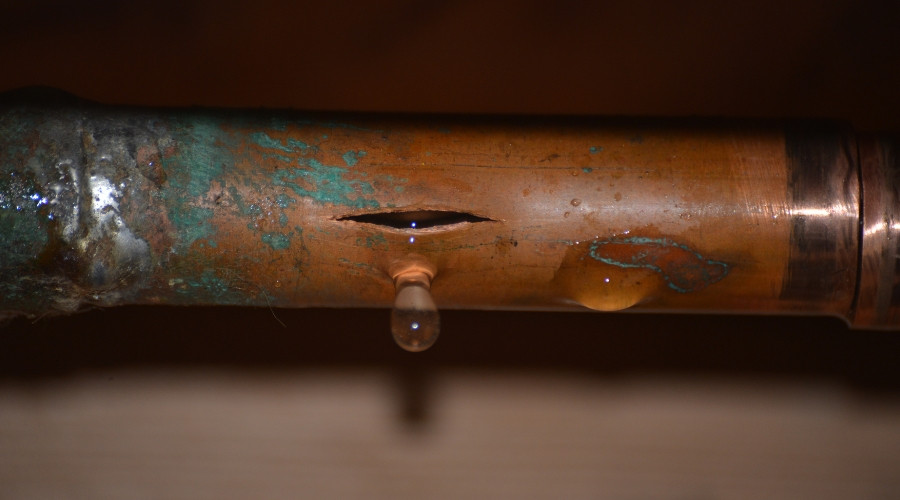 Copper pipe with visible water leak, showing corrosion and droplets forming at the crack, relevant to plumbing leak detection and repair.